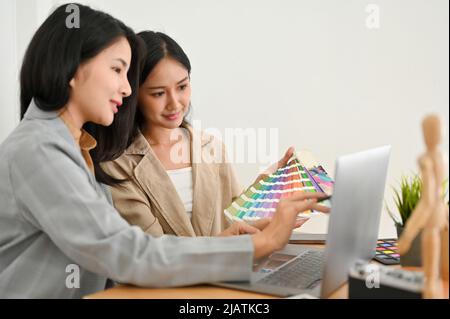 Zwei der schönen asiatischen jungen Grafikdesignerin sprechen, diskutieren und planen ihr grafisches Webbanner-Projekt gemeinsam im Büro. Stockfoto