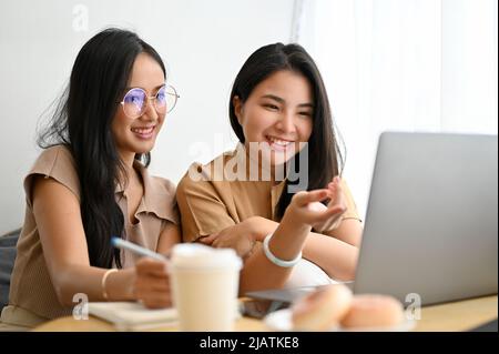 Schöne asiatische junge weibliche College-Studentin, die online studiert und mit ihrer College-Freundin im Café an einer Online-Klasse teilnehmen. Stockfoto