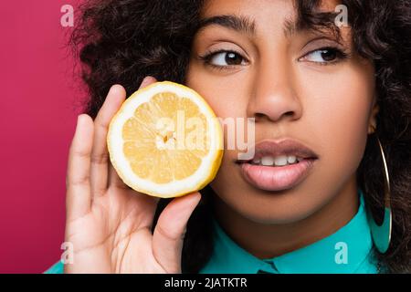 Nahaufnahme Porträt einer afroamerikanischen Frau mit einer halben Zitrone isoliert auf rosa Stockfoto