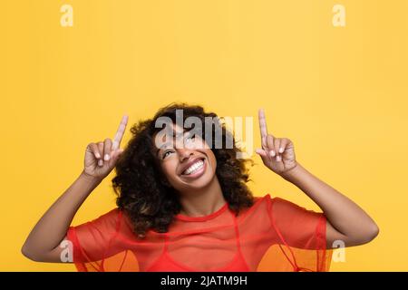 Lächelnde afroamerikanische Frau, die nach oben schaute und mit Fingern auf Gelb zeigte Stockfoto