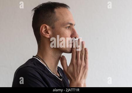 Fotomann sieht mit Interesse Ausdruck beiseite, hält die Hand in der Nähe der Lippen. Schöner junger Mann auf weißem Hintergrund in Studio mit leerem Raum isoliert Stockfoto