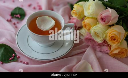 Eine Tasse Tee und ein Rosenstrauß auf rosa Hintergrund. Stockfoto