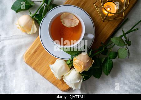 Eine Tasse Tee und ein Strauß Rosen auf weißem Hintergrund, warme und pastellfarbene Töne. Draufsicht. Stillleben Stockfoto