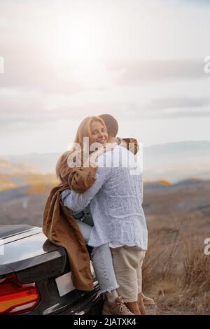 Vertikale Aufnahme einer schönen jungen blonden Frau, die ihren geliebten Mann im Freien umarmt Stockfoto