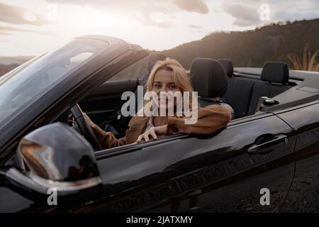Nahaufnahme einer fröhlichen jungen, schönen blonden Frau, die in einem Cabriolet vor der Kamera lächelt Stockfoto