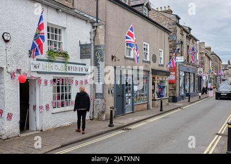 Eine Straße in einer hübschen Touristenstadt am Rande der Yorkshire Dales und des Lake District mit Schaufenstern und einem Shopper mit der Unionsflagge Stockfoto