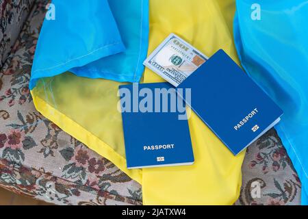 Biometrischer Auslandspass mit Geld liegt auf der Nationalflagge der Ukraine gelb-blau. Stockfoto