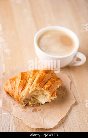 Bissen Sie Croissant und eine Tasse Cappuccino auf einem Holztisch. Frühstück oder Kaffeepause im Café Stockfoto