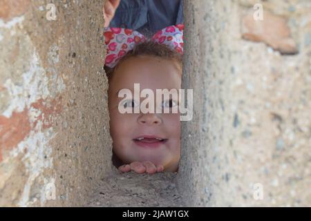 Kleines Mädchen, das durch ein Loch in der Wand guckt, Gebäude, Spanien, Espana Stockfoto