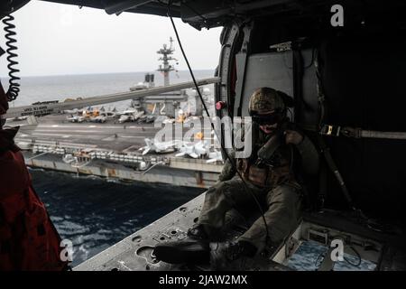 PHILIPPINISCHE SEE (20. Mai 2022) Naval Air Crewman (Hubschrauber) 2. Klasse Cole West, aus Kansas City, reitet in der Kabine eines MH-60s Sea Hawk Hubschraubers, der den „Chargers“ von Helicopter Sea Combat Squadron (HSC) 14 zugewiesen wurde, während eines Munitionsübergangs mit dem Flugzeugträger USS Abraham Lincoln der Nimitz-Klasse (CVN 72) und dem Flugzeugträger USS Ronald Reagan (CVN 76) der Nimitz-Klasse in einem. Die Abraham Lincoln Strike Group befindet sich im geplanten Einsatzbereich der US-Flotte für 7., um die Interoperabilität durch Allianzen und Partnerschaften zu verbessern und gleichzeitig als reaktionsfähige Truppe in s zu dienen Stockfoto