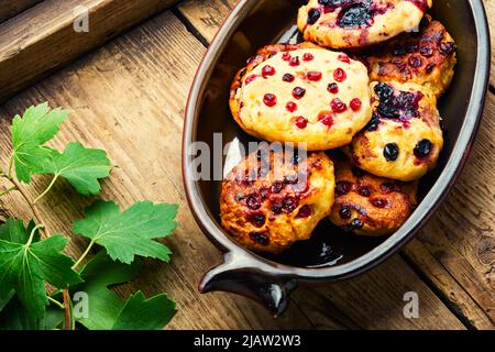 Hüttenkäse-Pfannkuchen oder Syrniki mit Sommerbeeren. Korbpfannkuchen mit roten und schwarzen Johannisbeeren auf einem ländlichen Holztisch Stockfoto