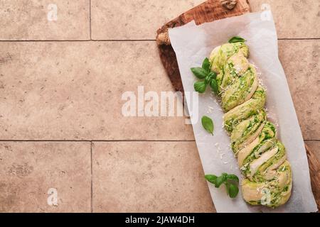 Geflochtenes Bärlauch-Pesto Brioche. Hausgemachtes rohes oder rohes, frisches Pull-Apart-Brot mit Bärlauch-Pesto auf Holzbrett auf alten beigefarbenen Fliesen Stockfoto