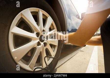 Frau bläst den Reifen auf. Frau, die den Reifendruck überprüft und Luft in den Reifen des Autorads pumpt. Autowartung zur Sicherheit vor der Reise. Ti Stockfoto