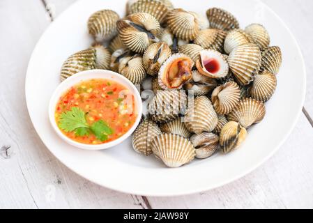 Herzmuscheln auf weißem Teller mit Meeresfrüchte-Sauce auf dem Tischhintergrund, frische rohe Schalentiere Blut Herzmuschel Ozean Gourmet Meeresfrüchte im Restaurant Stockfoto