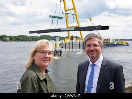 01. Juni 2022, Brandenburg, Werder (Havel): Manuela saß (CDU), Bürgermeisterin von Werder (Havel), und Mike Schubert (SPD), Bürgermeister (ob) von Potsdam, stehen auf einem Steg, dahinter hängt der mittlere Teil einer Brücke am Ausleger eines schwimmenden Krans, der auf dem Großen Zernsee fährt. Die künftige Fahrrad- und Fußgängerbrücke zwischen Werder und Potsdam soll am 2. Juni 2022 fertiggestellt werden, wenn der letzte Stahlaufbauten-Abschnitt und die Aussichtsplattform angehoben werden. Foto: Soeren Sache/dpa Stockfoto