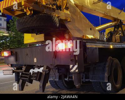 Ein gelb-schwarzer LKW-Kran mit Scheinwerfern steht auf der Nachtstraße. Straßenarbeiten Stockfoto