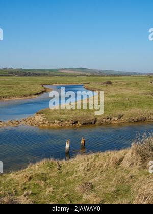 Ein sonnenbeschienenen Fluss schlängelt sich durch die offenen Felder eines Feuchtgebiets mit sanften Hügeln am Horizont und einem sommerlich blauen Himmel über dem Himmel. Stockfoto