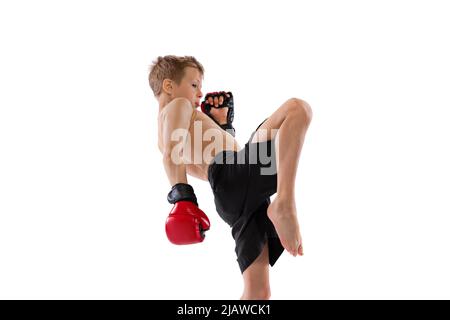 Dynamisches Porträt eines kleinen Jungen, eines Kindes in Sportaufnahmen und Handschuhe, die Thai-Boxen auf weißem Studiohintergrund üben. Sport, Bildung, Action, Bewegung Stockfoto