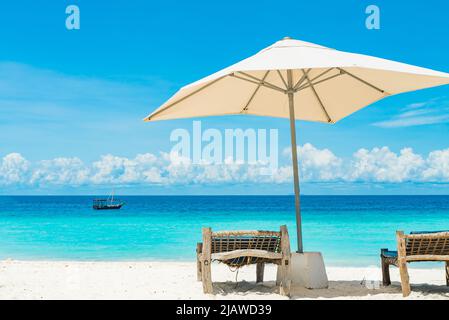 Liegestühle aus Holz an einem Sandstrand vor dem Meer mit Booten, Sansibar Tansania Stockfoto