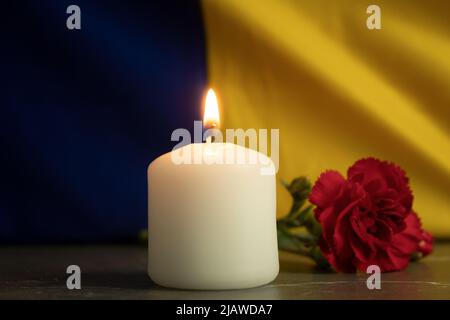 Eine brennende Kerze vor dem Hintergrund der Nationalflagge der Ukraine. Hintergrund mit Kopierbereich. Gedächtniskerze, Erinnerung und Trauer Stockfoto