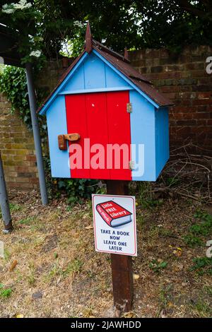 Die Offords Little Free Library, Buchwechselbox auf dem Postweg. Blau mit roter Tür. Offord Cluny, Cambridgeshire, England Stockfoto