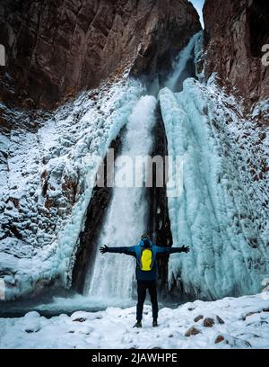 Tourist spreizte seine Arme Blick von der Rückseite eines teilweise gefrorenen Wasserfall Stockfoto