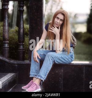 Eine langhaarige Frau sitzt am Sommernachmittag auf dem Marmorkandon der Straßentreppe. Stockfoto