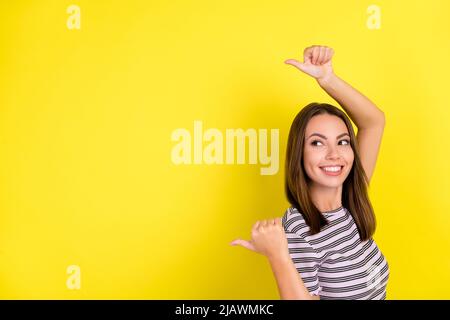 Foto von niedlichen tausendjährigen Brünette Dame Punkt leeren Raum tragen gestreiften T-Shirt auf gelbem Hintergrund isoliert Stockfoto