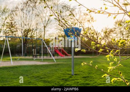 Spielplatz im öffentlichen Park an einem sonnigen Frühlingstag mit grünem Gras und Bäumen. Stockfoto