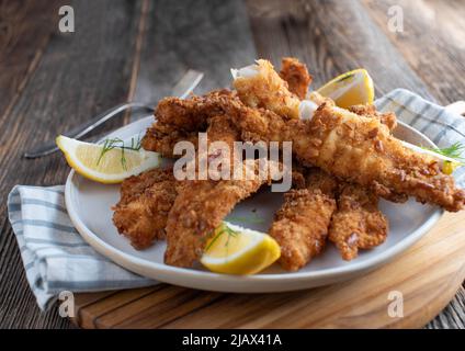 Knusprig gebratener Fisch auf einem Teller mit Zitrone. Auf Holztisch isoliert serviert. Nahaufnahme mit Kopierbereich Stockfoto