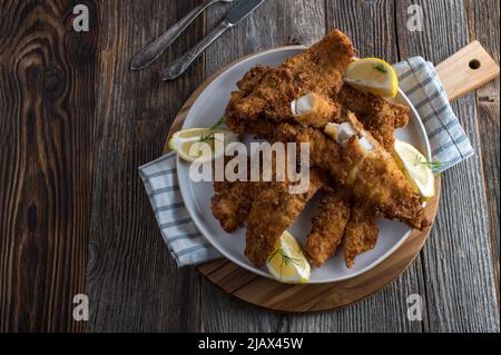 Frittiertes Fischfilet mit Brezelbreadierung. Serviert auf einem Teller mit Zitrone isoliert auf Holztisch Hintergrund. Draufsicht Stockfoto