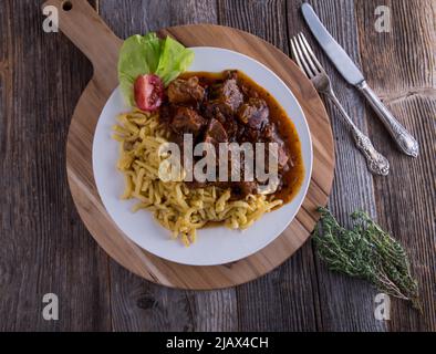 Gulasch mit spätzle Nudeln auf einem Teller isoliert auf Holztisch mit Kopieplatz Stockfoto