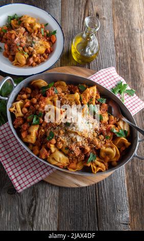 Italienische Pasta mit Tortellini, Pancetta, Kichererbsen, Gemüse und Tomatensauce. Garniert mit Parmesankäse und in einer rustikalen Pfanne serviert Stockfoto
