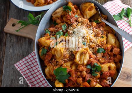 Pasta mit Tomatensauce, Kichererbsen, Pancetta, Gemüse und Parmesankäse. Serviert in einer rustikalen Pfanne auf Holztisch Hintergrund. Draufsicht Stockfoto