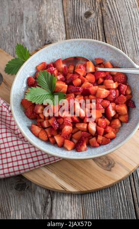 Erdbeerdessert mit frisch gehackten und marinierten Erdbeeren. Serviert in einer Schüssel mit Löffel auf Holztisch mit Kopierplatz Stockfoto