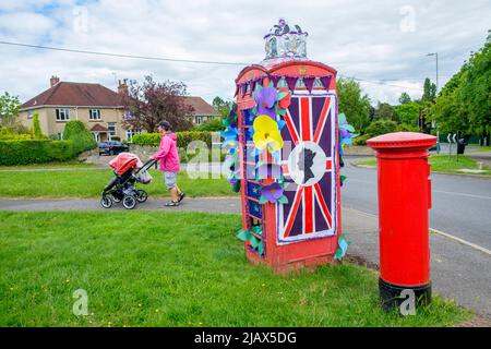 Chippenham, Wiltshire, Großbritannien. 1.. Juni 2022. Einen Tag vor Beginn des langen Feiertagswochenendes wird ein Mann abgebildet, der ein Kind in einem Buggy schiebt, während er an einer Telefonbox vorbeigeht, die zur Feier des Platin-Jubiläums der Königin dekoriert wurde. Quelle: Lynchpics/Alamy Live News Stockfoto