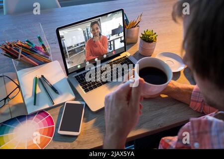 Kaukasischer Geschäftsmann, der während eines Videoanrufs mit einer lächelnden afroamerikanischen Kollegin Kaffee getrunken hat Stockfoto