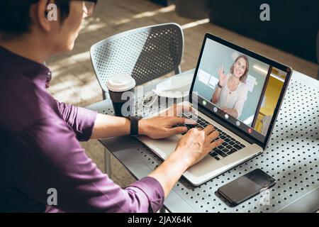 Asiatischer Geschäftsmann, der im Café einen Laptop benutzt, während er mit einem kaukasischen Kollegen bei einem Videoanruf zusammenarbeitete Stockfoto