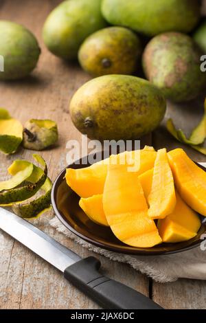 Mangoscheiben auf einem Teller mit ganzen Mangos im Hintergrund, aufgenommen in geringer Schärfentiefe Stockfoto