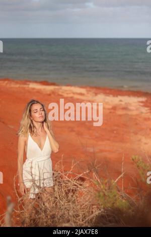 Schöne junge blonde Frau in weißem Kleid am roten Sandstrand an der Westküste Australiens Stockfoto