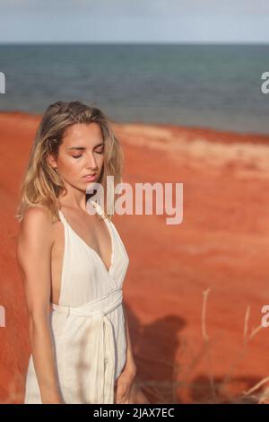 Nahaufnahme Porträt der schönen jungen blonden Frau in weißem Kleid am roten Sandstrand an der Westküste Australiens Stockfoto