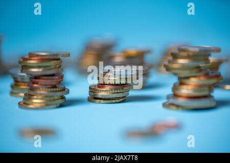 Auf blauem Hintergrund stapelten sich Münzen. Euro-Münzen aus der Europäischen Union. Geld und Bargeld stapelten sich bis zu Türmen Stockfoto