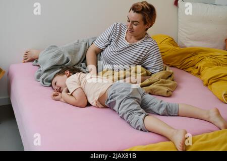 Mutter hat Spaß mit Sohn auf dem Bett. Mutter und Kleinkind spielen, kitzeln ein Kind, lachen am Morgen. Positive Emotionen nach dem Schlaf. Aufwachendes Kind Stockfoto