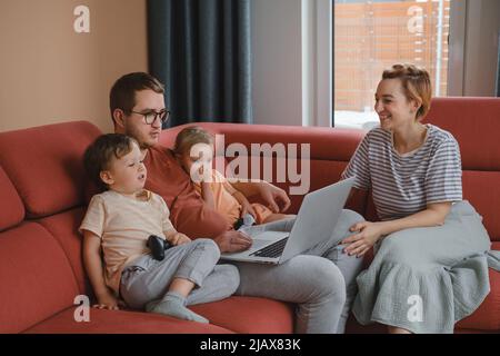 Große glückliche Familie, die Filme und Spiele auf einem Laptop ansieht. Mutter Vater Kinder verbringen Zeit mit Gadgets auf dem Sofa Kinder mit Eltern suchen auf Stockfoto