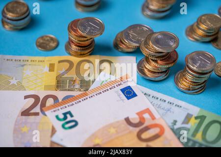 Euro-Münzen neben Euro-Banknoten aufgeschichtet. Währung der Europäischen Währungsunion. Bargeld auf blauem Hintergrund, Papierrechnungen und Münzen, die über 200 emporragen Stockfoto