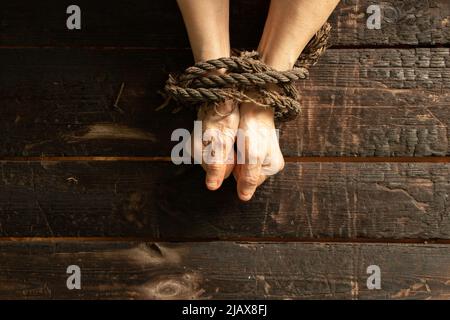 Gefesselt die Hände einer alten Frau mit einem Seil auf einem Holztisch, Mangel an Macht über die Menschen, Sklave Stockfoto