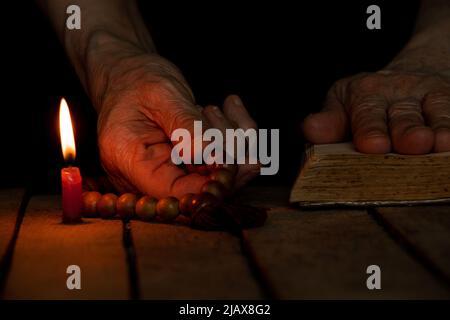 Eine Frau mit einem hölzernen Rosenkranz und einer bibel erbrach Kerzen im Dunkeln, eine Frau betet, betet, Glaube und Religion,Tempel Stockfoto