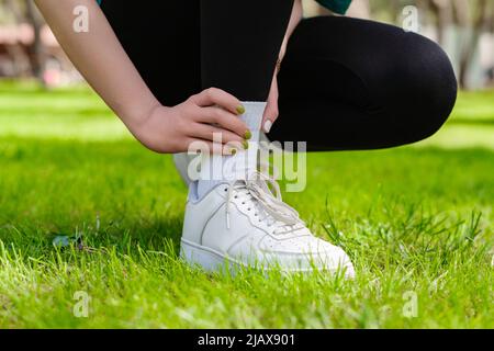 Nahaufnahme einer jungen Läuferin, die schwarze Leggings trägt und beim Training und Laufen an einem Knöchel verletzt ist. Gesundheits- und Sportkonzept. Stockfoto