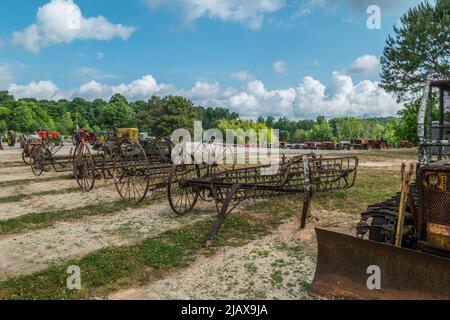 Eine Sammlung von alten landwirtschaftlichen Maschinen Vintage-Traktoren und eine kleine Bulldozer alle in Reihen in einem offenen Feld auf Ackerland mit den Wäldern im Bac geparkt Stockfoto