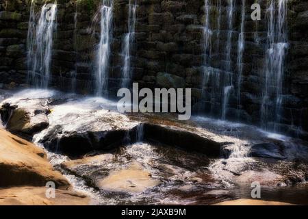 Wasser überläuft den Felsdamm auf die Felsen unterhalb des Yates Mill County Park in North Carolina. Stockfoto